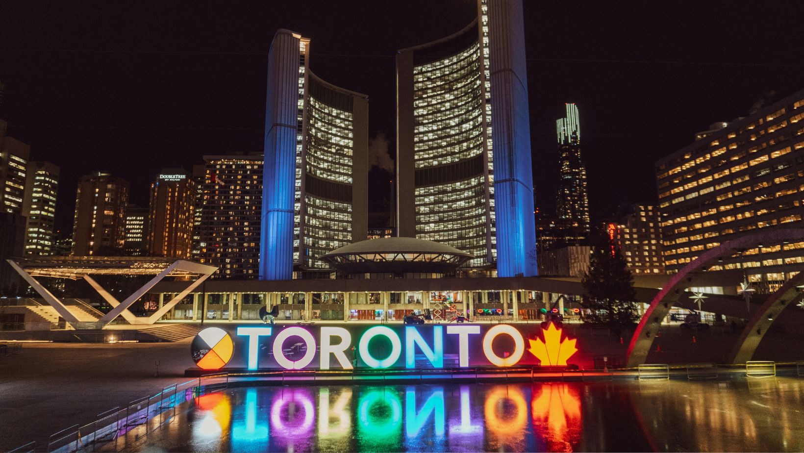 Big buildings and a huge neon Toronto sign at nighttime depicting career opportunities for interior designers in Canada's top cities