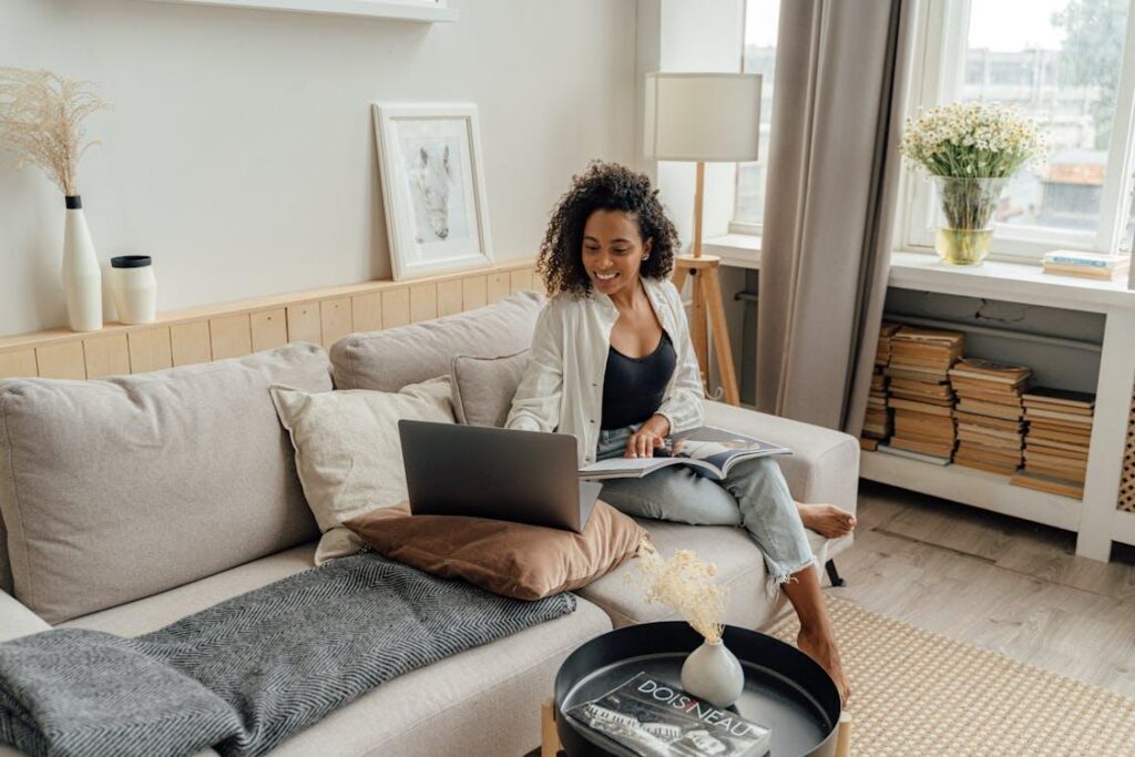 Free Woman in White Long Sleeve Using a Laptop while Sitting on a Sofa Stock Photo